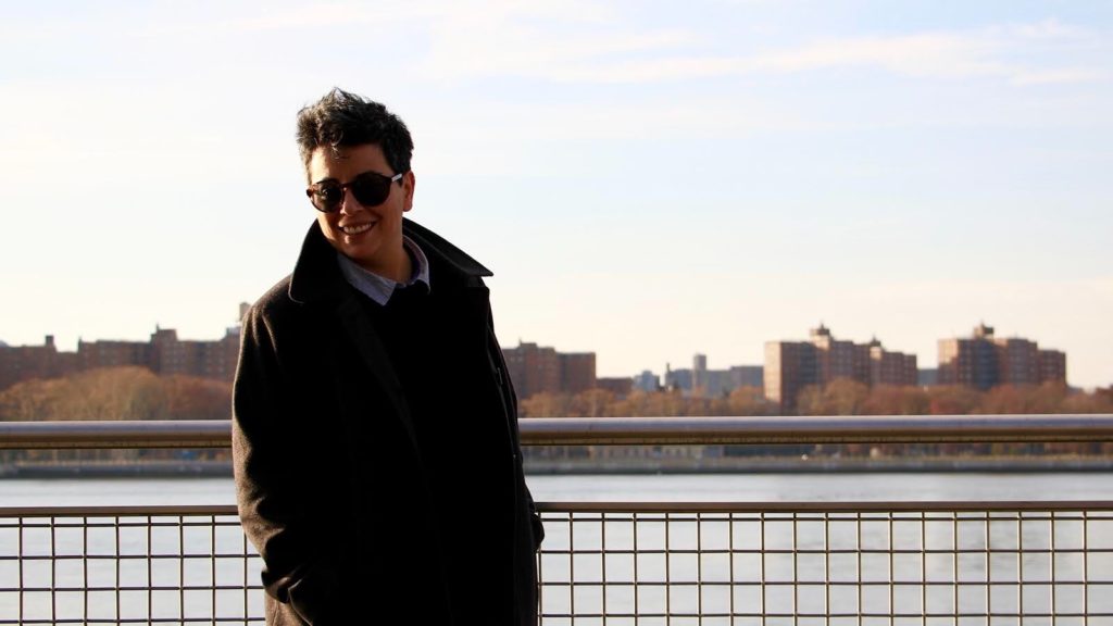 Ilon smiling looking towards the ground, with a landscape and lake behind them