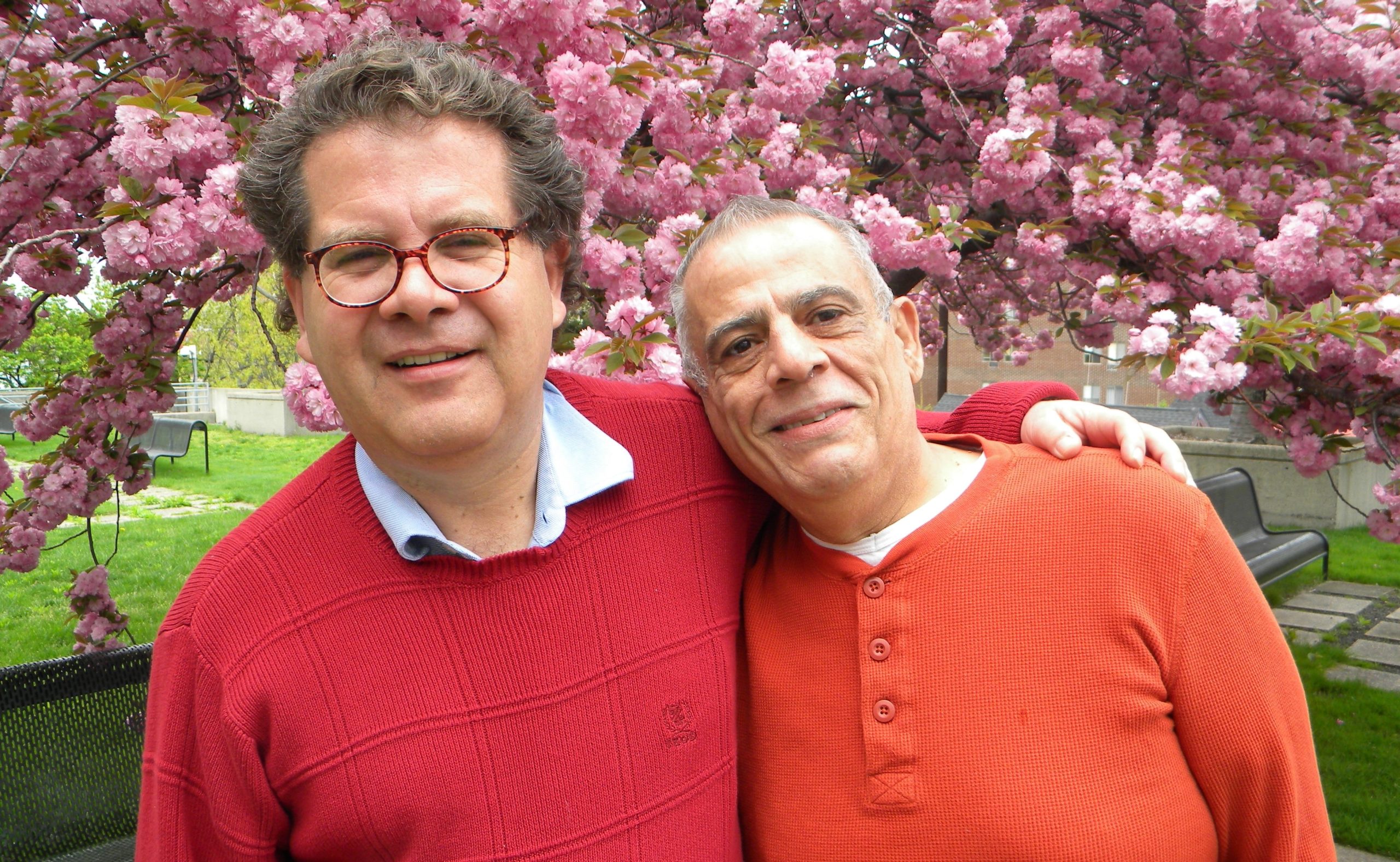 Santiago and Pablo hugging in front of a pink blossoming tree with colorful sweaters on