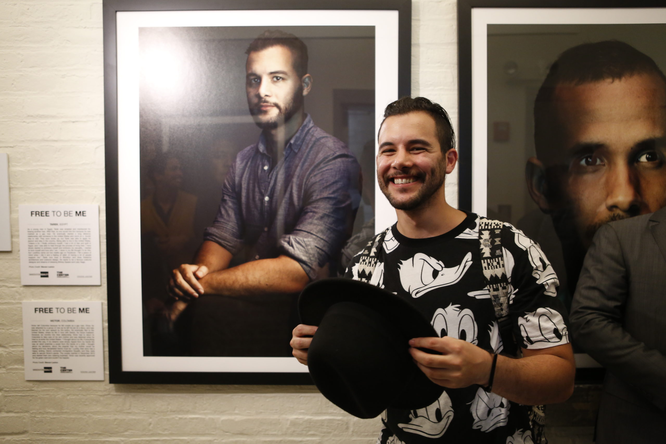 Tarek smiling in front of a large portrait photograph, whilst holding his hat