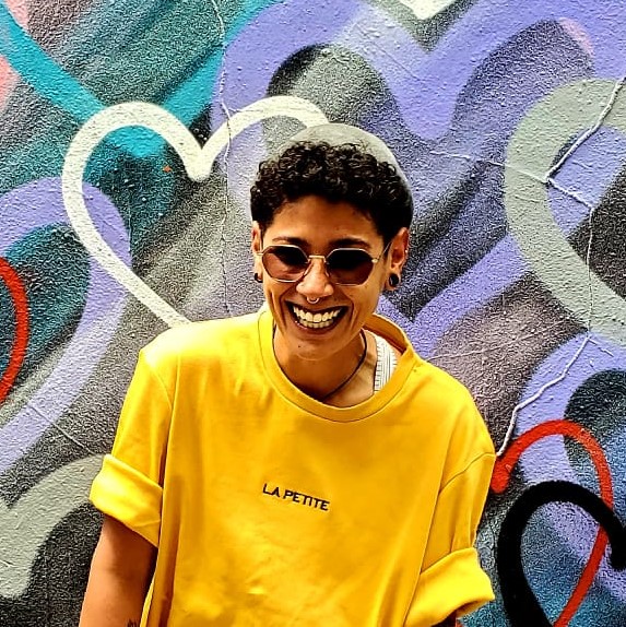 Jude joyously smiling with a yellow t-shirt, in front of a mural covered with a variety of hearts